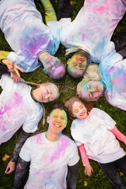 Holi 'yi pudra rengi ya da gulal ile kutlayan bir grup mutlu insan. Çimlerin üzerinde uzanmış, manzarası güzel. Hint festivali Holi kavramı.