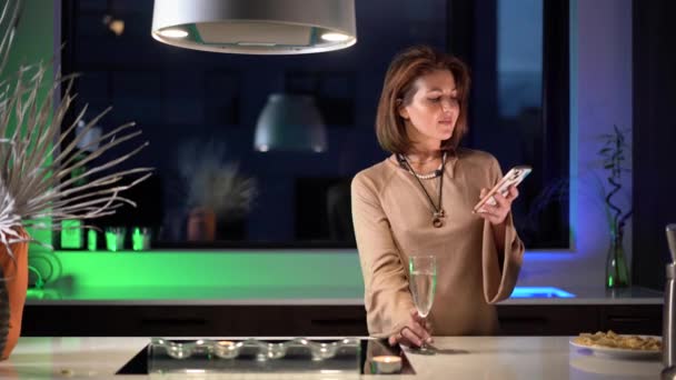 一位在厨房里拿着电话的女性正在家里等待着电话和穿着节日礼服的浪漫对话 背景是绿色灯光下的4K视频 — 图库视频影像