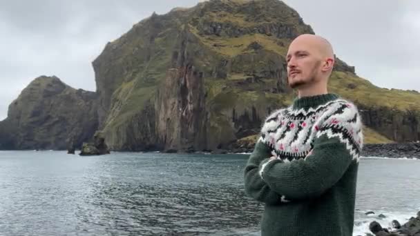 一个年轻的秃头小伙子穿着一件冰岛毛衣站在海边的背景上 英俊的白人男子4K型镜头 — 图库视频影像