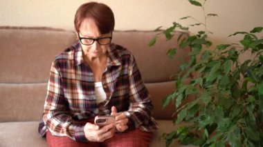 Seksen yaşında bir kadın elinde telefon, evde çalışıyor. Telefonla ellerin yakın plan görüntüsü