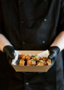 Aşçı elinde içinde ızgara tavuk teriyaki bacakları olan bir kutu tutuyor.. 