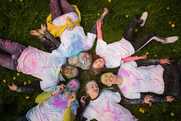 Group of happy people celebrating Holi with powder colors or gulal. Lying on the grass, top view. Concept of Indian festival Holi.