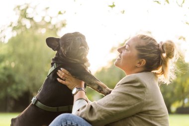 Kırk yaşında sarışın bir kız, köpeğine sarılıyor, bir Fransız bulldog, çimlerin üzerinde bir parkta..