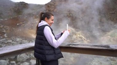 Kız turist, İzlanda doğası ve kaplıcalarının telefonuyla fotoğraf çekiyor.