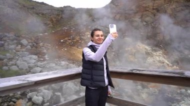 Kız turist, İzlanda doğası ve kaplıcalarının telefonuyla fotoğraf çekiyor.