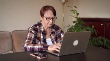 Yaşlı kadın 80 yaşında dizüstü bilgisayarla evde çalışıyor.