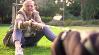 40 'lı yaşlarda bir kadın, köpeği Fransız bulldog' la parkta çimlerin üzerinde oynuyor. 4K görüntülerinde.