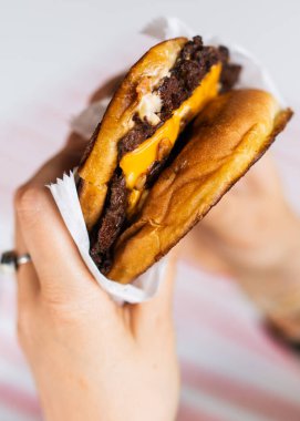 Adam elinde bir hamburger, masada kola ve patates kızartması tutuyor.