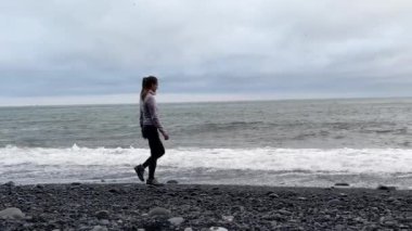 Kız, Vik, İzlanda 'nın kara plajı yakınlarında okyanus kenarında yürüyor.