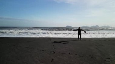 Siyah elbiseli ve dizüstü bilgisayarlı bir kız İzlanda 'da siyah bir plaj boyunca yürüyor. Özgürlük ve serbest dolaşım kavramı, İHA 'nın 4K görüntüsü.