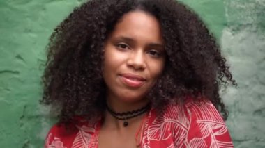 Havalı Afro-Amerikalı bir kız turkuaz arka planda kırmızı bir elbise giyiyor ve gülümsüyor.