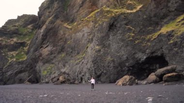 Bir kız İzlanda 'da siyah bir sahilde yürüyor ve selfie çekiyor.