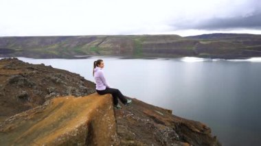 Kız İzlanda dağlarında gölün kenarında oturuyor.