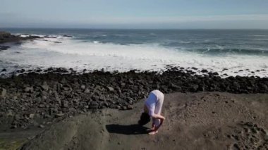 Okyanus kıyısındaki bir kayanın üstünde yoga yapan bir kız, gün batımında İzlanda 'da bir dronun manzarası.