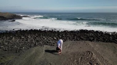 Okyanus kıyısındaki bir kayanın üstünde yoga yapan bir kız, gün batımında İzlanda 'da bir dronun manzarası.
