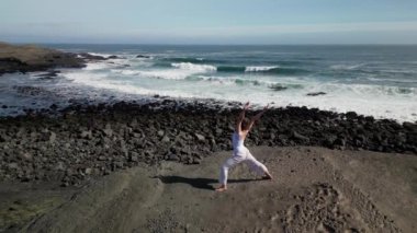 Okyanus kıyısındaki bir kayanın üstünde yoga yapan bir kız, gün batımında İzlanda 'da bir dronun manzarası.