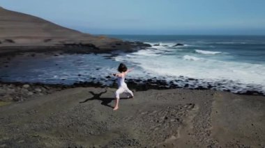 Okyanus kıyısındaki bir kayanın üstünde yoga yapan bir kız, gün batımında İzlanda 'da bir dronun manzarası.