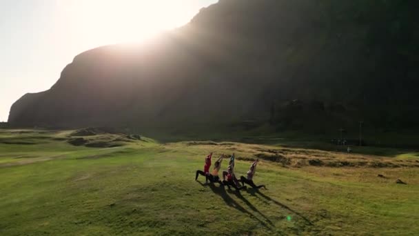 日没のヨガ教室 ヨガツリーを練習する若者の幸せな多様なグループが一緒にポーズし 山で健康とウェルネスを伸ばし ドローンから撮影 — ストック動画