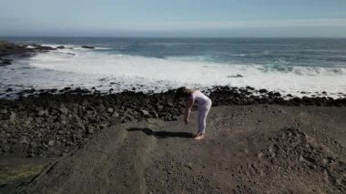 Okyanus kıyısındaki bir kayanın üstünde yoga yapan bir kız, gün batımında İzlanda 'da bir dronun manzarası.