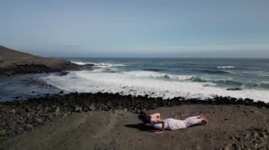 Okyanus kıyısındaki bir kayanın üstünde yoga yapan bir kız, gün batımında İzlanda 'da bir dronun manzarası.