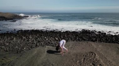Okyanus kıyısındaki bir kayanın üstünde yoga yapan bir kız, gün batımında İzlanda 'da bir dronun manzarası.