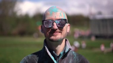 Holi 'yi kutlayan ve kameraya bakan pudra renkli sakallı ve bıyıklı bir portre adam. Kapat.