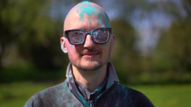 Holi 'yi kutlayan ve kameraya bakan pudra renkli sakallı ve bıyıklı bir portre adam. Kapat.