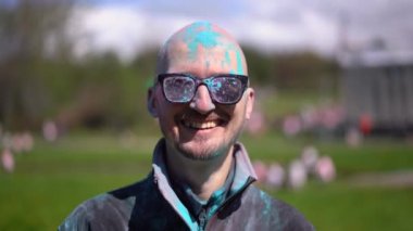 Holi 'yi kutlayan ve kameraya bakan pudra renkli sakallı ve bıyıklı bir portre adam. Kapat.