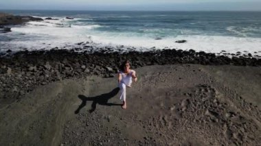 Okyanus kıyısındaki bir kayanın üstünde yoga yapan bir kız, gün batımında İzlanda 'da bir dronun manzarası.