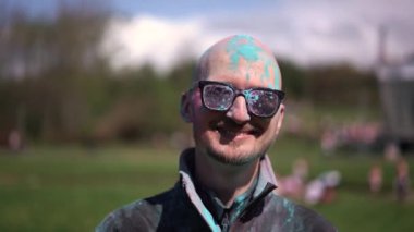 Holi 'yi kutlayan ve kameraya bakan pudra renkli sakallı ve bıyıklı bir portre adam. Kapat.