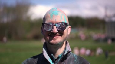 Holi 'yi kutlayan ve kameraya bakan pudra renkli sakallı ve bıyıklı bir portre adam. Kapat.