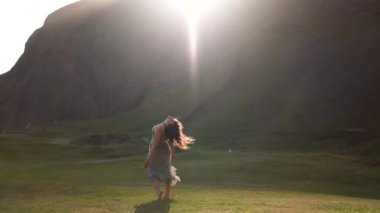 Yeşil elbiseli bir kız gün batımında İzlanda 'da bir tarlada dans eder.