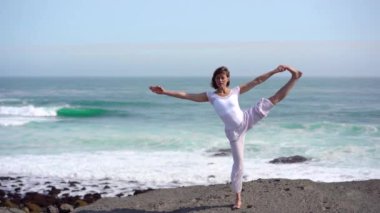 Okyanus kıyısındaki bir kayanın üstünde yoga yapan bir kız, gün batımında İzlanda 'da bir dronun manzarası.