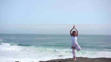 Okyanus kıyısındaki bir kayanın üstünde yoga yapan bir kız, gün batımında İzlanda 'da bir dronun manzarası.