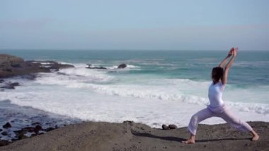 Okyanus kıyısındaki bir kayanın üstünde yoga yapan bir kız, gün batımında İzlanda 'da bir dronun manzarası.
