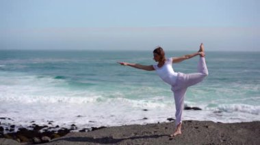 Okyanus kıyısındaki bir kayanın üstünde yoga yapan bir kız, gün batımında İzlanda 'da bir dronun manzarası.