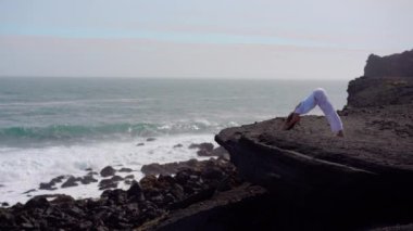 Okyanus kıyısındaki bir kayanın üstünde yoga yapan bir kız, gün batımında İzlanda 'da bir dronun manzarası.