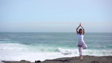 Okyanus kıyısındaki bir kayanın üstünde yoga yapan bir kız, gün batımında İzlanda 'da bir dronun manzarası.