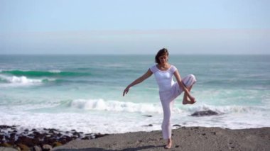 Okyanus kıyısındaki bir kayanın üstünde yoga yapan bir kız, gün batımında İzlanda 'da bir dronun manzarası.