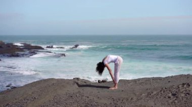 Okyanus kıyısındaki bir kayanın üstünde yoga yapan bir kız, gün batımında İzlanda 'da bir dronun manzarası.
