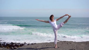 Okyanus kıyısındaki bir kayanın üstünde yoga yapan bir kız, gün batımında İzlanda 'da bir dronun manzarası.