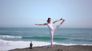 Okyanus kıyısındaki bir kayanın üstünde yoga yapan bir kız, gün batımında İzlanda 'da bir dronun manzarası.