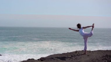 Okyanus kıyısındaki bir kayanın üstünde yoga yapan bir kız, gün batımında İzlanda 'da bir dronun manzarası.