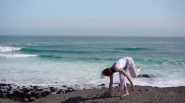 Okyanus kıyısındaki bir kayanın üstünde yoga yapan bir kız, gün batımında İzlanda 'da bir dronun manzarası.