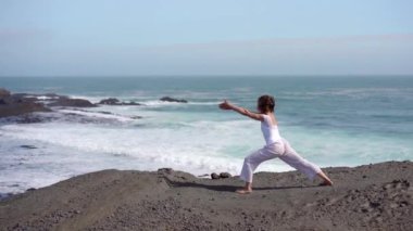 Okyanus kıyısındaki bir kayanın üstünde yoga yapan bir kız, gün batımında İzlanda 'da bir dronun manzarası.