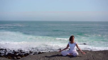 Okyanus kıyısındaki bir kayanın üstünde yoga yapan bir kız, gün batımında İzlanda 'da bir dronun manzarası.