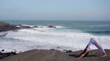 Okyanus kıyısındaki bir kayanın üstünde yoga yapan bir kız, gün batımında İzlanda 'da bir dronun manzarası.