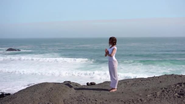 海の近くの岩の上にヨガをしている少女 日没のアイスランドの無人機からの眺め — ストック動画