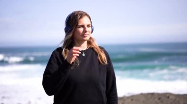 Kulaklıklı kız İzlanda 'da okyanusun arka planında müzik dinliyor.
