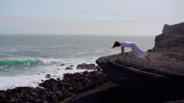 Okyanus kıyısındaki bir kayanın üstünde yoga yapan bir kız, gün batımında İzlanda 'da bir dronun manzarası.
